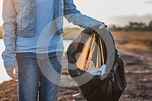 people volunteer keeping garbage plastic and glass bottle into black bag at park river in sunset