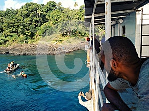 people waiting on a cargo boat next to a stunning tropical island while it uploads with a local outrigger canoe