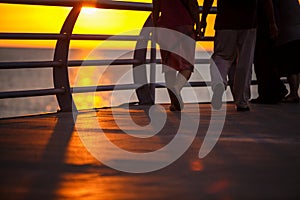 People walk along the promenade in the yellow and orange rays of the sun at sunset.