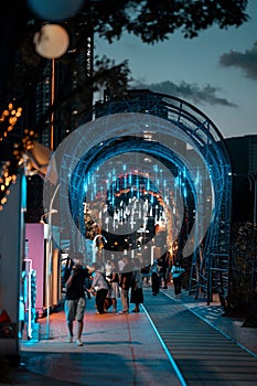 people walk along the street near the neon blue lights that create a tunnel