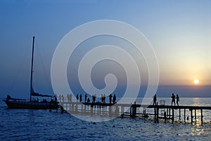 People walk on pier on sunset