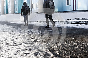 People walk on a slippery road made of melted ice. View of the legs of a man walking on an icy pavement. Winter road in the city.