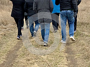 People are walking along a country road, rear view. The legs of men and women on the background of a dirt road. Concept: Cross