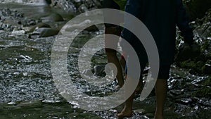 People walking barefeet in rocky mountainous river. Creative Summer hiking, cold stream in forest.