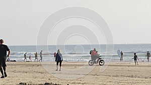 People walking on beach. Surfer men with surfboard going surfing. Family riding bike, California USA