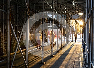 People walking down a sidewalk in New York City with the light of sunset shining through construction scaffolding