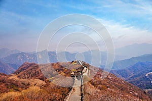 People walking on the Mutianyu section of the Great Wall of China, surrounded by green and yellow vegetation under a