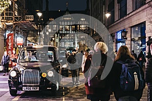 People walking past black cabs parked on Argyll Street, London, UK