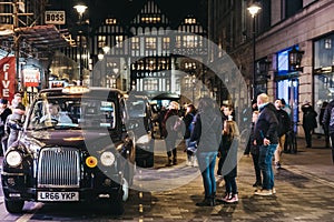 People walking past black cabs parked on Argyll Street, London, UK