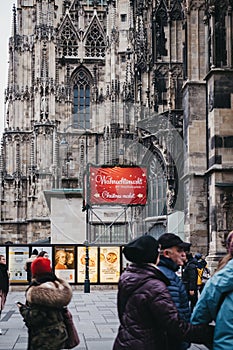 People walking past directional sign to Christmas market stall near St. Stephen Cathedral, Vienna, Austria.