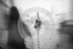 People walking in rainy weahtre look through window covered with drops of water