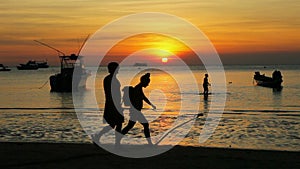 People walking on sea beach against sunset sky