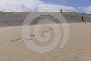 People walking up sand dunes on a bright sunny day in the desert