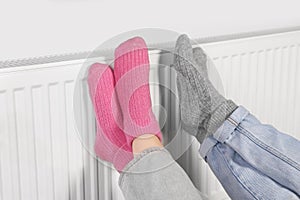 People warming feet near heating radiator, closeup