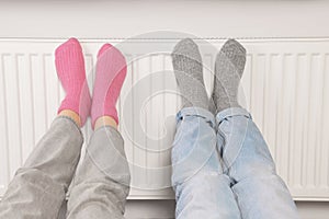 People warming feet near heating radiator, closeup