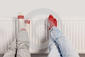 People warming feet near heating radiator indoors, closeup