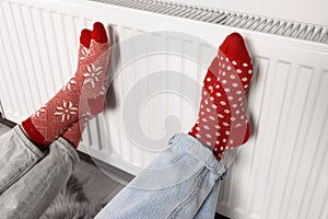 People warming feet near heating radiator indoors, closeup