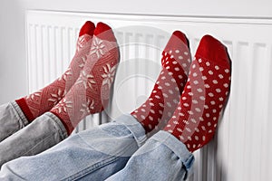 People warming feet near heating radiator indoors, closeup