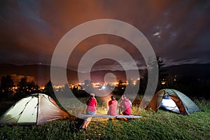 People watching fire together beside camp and tents in dark