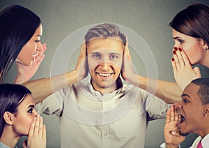 People whispering a secret gossip to a man who covers ears ignoring them photo