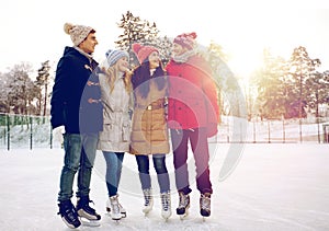 Happy friends ice skating on rink outdoors