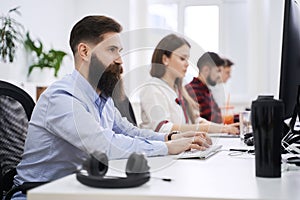 People working in modern IT office. Group of young and experienced programmers and software developers sitting at desks