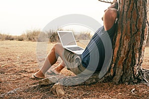 People working outdoor with computer and wireless connection. One man stretching his back against a tree with laptop on the legs.