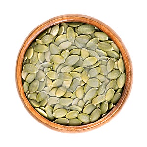 Pepitas, hulled pumpkin seeds after shelling, in a wooden bowl photo