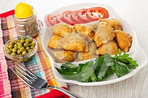 Pepper, bowl with green peas, fork on napkin, partitioned dish with patties, parsley, slices of tomato on wooden table