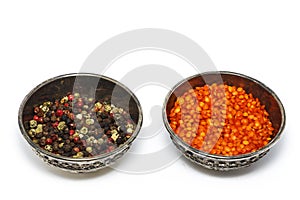 Pepper grains are red, black, white spices, float in a silver bowl. View from above. Isolated on white background.