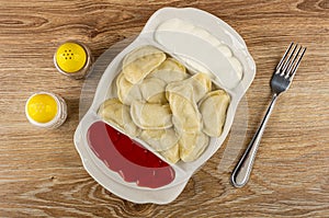 Pepper and salt, partitioned dish with dumplings, sour cream and ketchup, fork on table. Top view