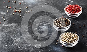 Pepper set. Black, white and pink rose peppers in bowls, assorted spices on gray kitchen table, selective focus