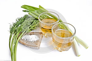 Pepper vodka in two transparent glasses, green onions, dill, rye bread and coarse salt - still life