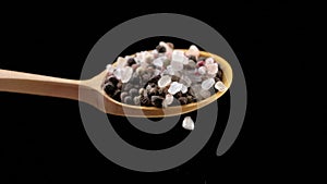 Peppercorn and salt falling from a wooden spoon