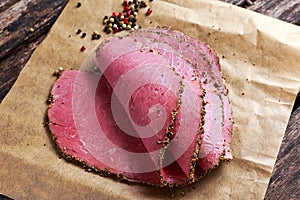 Peppered roast beef slices on paper with grains of coloured pepper.