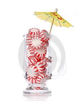 Peppermint candy in glass and cocktail umbrella isolated on white. Concept. Red striped mint Christmas candy