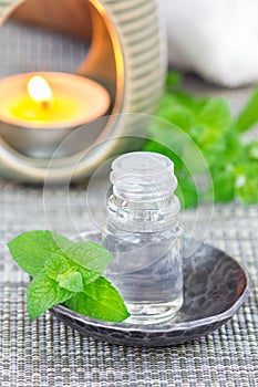 Peppermint essential oil in glass on gray mat with spa background