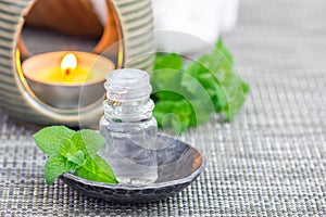 Peppermint essential oil in glass on gray mat with spa background, copy space