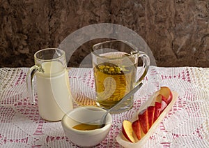 Peppermint tea, with floating mint leaves, in a clear glass cup, a jug with cow`s milk, red apple