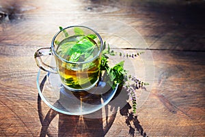 Peppermint tea from fresh leaves and flowering twigs in a glass cup, refreshment and herbal medicine on a rustic wooden table,