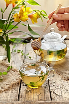 Peppermint tea with honey in glass cup, teapot and flowers