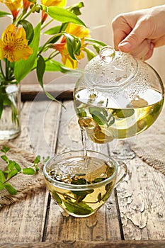 Peppermint tea pouring in glass cup from teapot on table