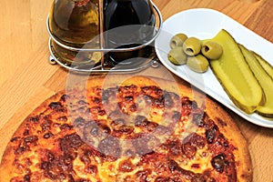 A pepperoni pizza with pickle and olives as a side