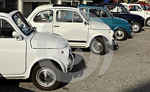 Row of white and blue vintage Fiat 500 at the roadside during a collector's car gathering.