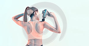 Percussion massager, sports young brunette female massaging shoulder in neon studio light, therapy for joint pain relief