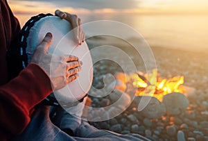 Percussionist plays djembe on the seashore near fire, hands close up