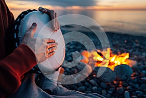 Percussionist plays djembe on the seashore near fire, hands close up