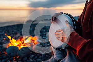 Percussionist plays djembe on the seashore near fire, hands close up