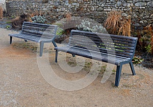 Perennial bed mulched with gray gravel in front of a limestone stone wall in a square with benches with wood paneling, beige path