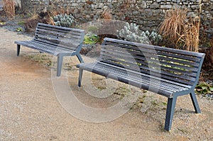 Perennial bed mulched with gray gravel in front of a limestone stone wall in a square with benches with wood paneling, beige path